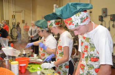 Three young teens in decorative aprons, cooking together. 