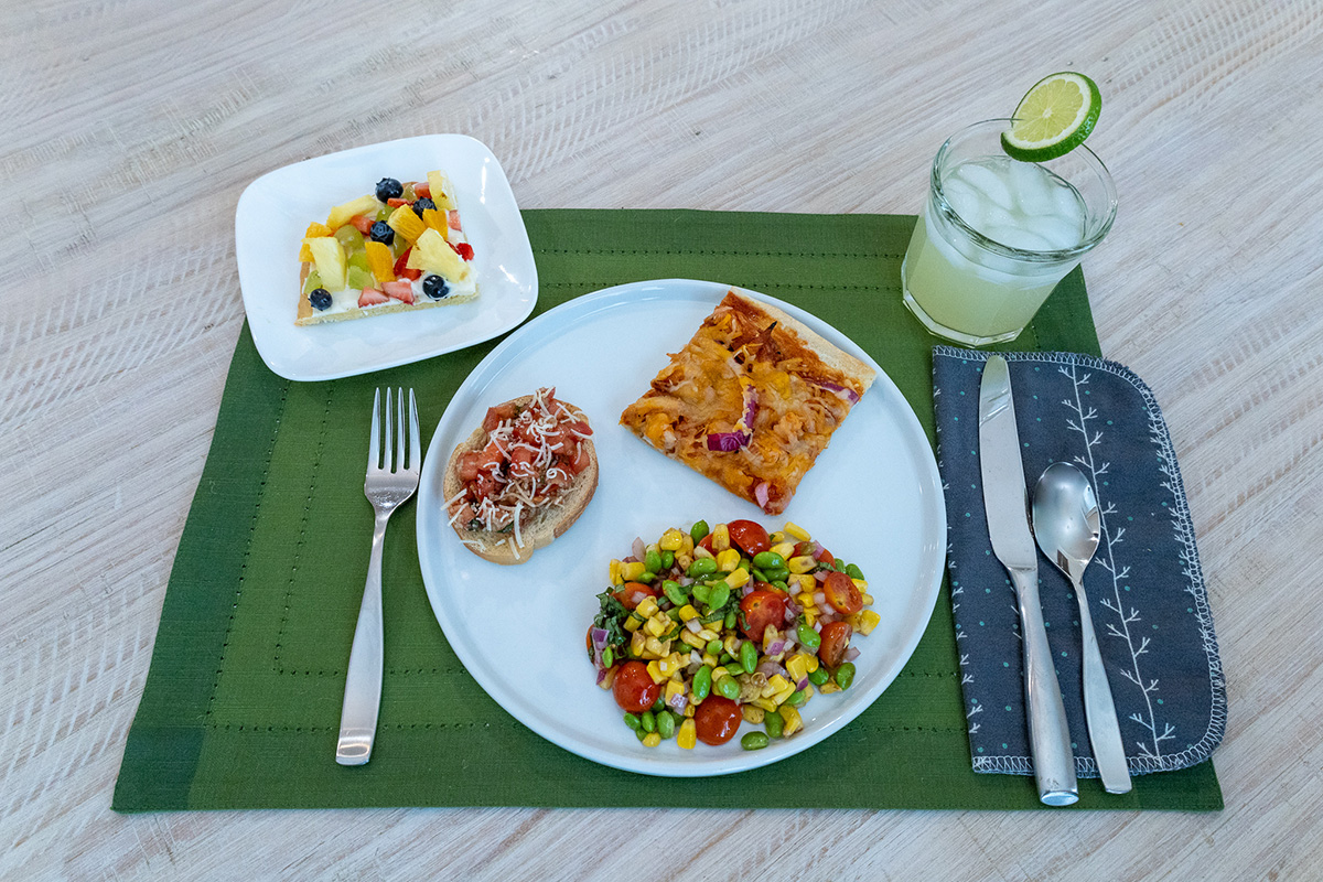A plate on a table with chicken pizza, fruit, and a cinnamon roll A plate on a table with chicken pizza, fruit, and a cinnamon roll